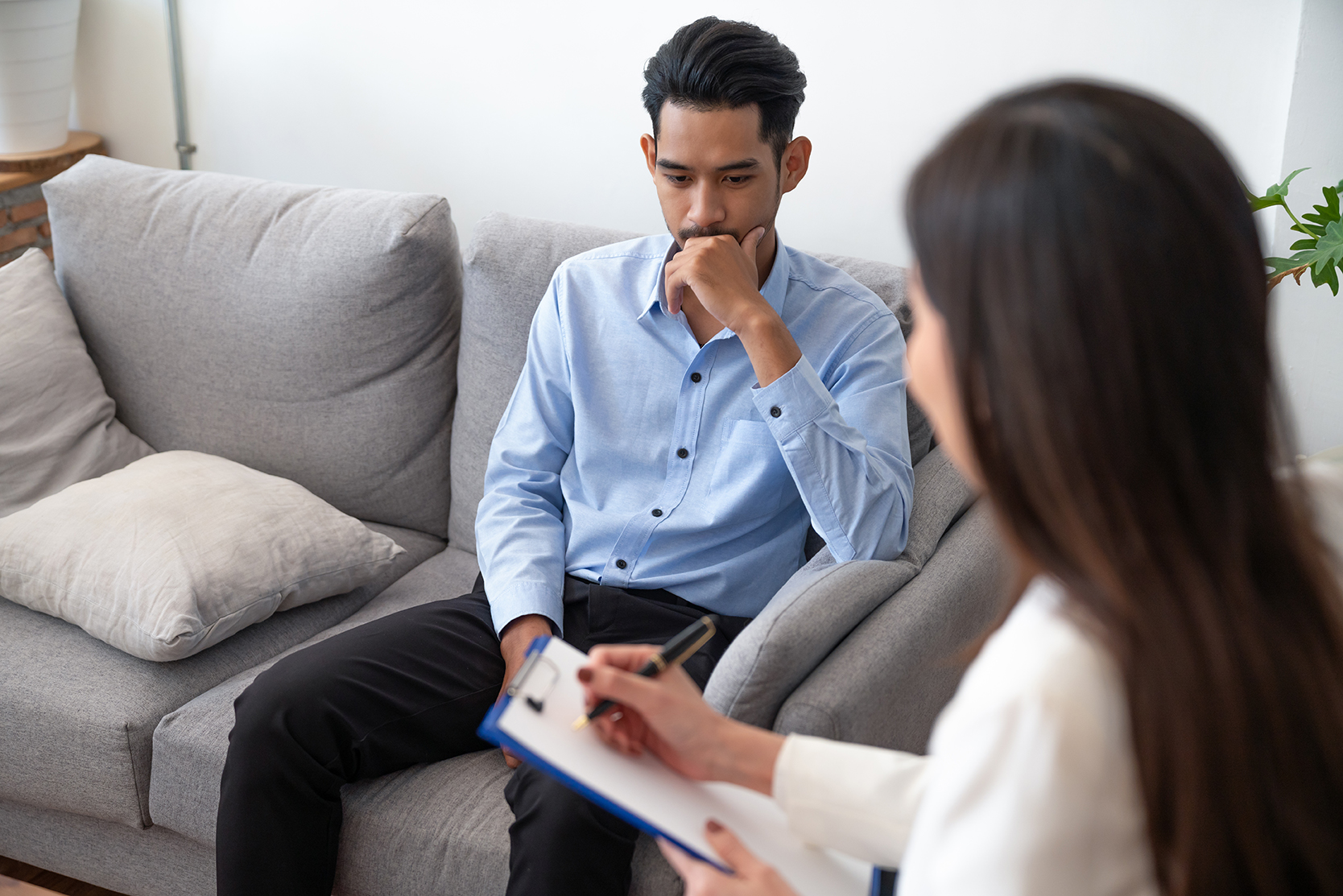 Woman psychiatrist writing information of asian young man patient while talking about his illness.